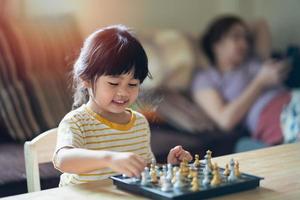 Little asian baby playing chess in the living room at home.Smart kid.fashion children. Little genius Child. Intelligent game.Chessboard. Baby activity concept. photo
