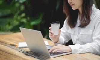 Business woman working on laptop and holding cup hot coffee on wooden table with a cup of coffee. Business concept work form home anywhere. photo