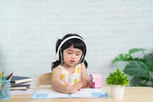 Cute little child wearing white headphone painting with colorful paints. Asian girl using wood color drawing color.Baby artist activity lifestyle concept. photo