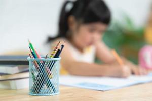 close up pencil holder and cute little child wearing white headphone painting with colorful paints. Asian girl using wood color drawing color.Baby artist activity lifestyle concept. photo