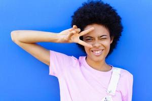 Cheerful black woman making peace sign near wall photo