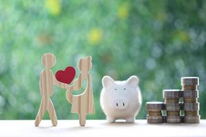 Love couple holding heart shape with piggy bank and stack of coins money on natural green background,Save money for prepare in future and family finance concept photo