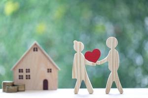 Love couple holding heart shape and stack of coins money with model house on natural green background, Saving for lover or family and save money for prepare in future concept photo