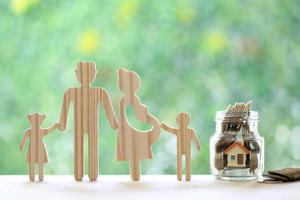 familia feliz con casa modelo y moneda de oro en la botella de vidrio sobre fondo verde natural, ahorre dinero para prepararse en el futuro y el concepto de bebé recién nacido foto