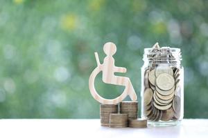 Man on wheelchair and gold coin money in the glass bottle on natural green background,Save money for prepare in future and handicapped person concept photo