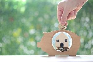 Stack of coins money in piggy bank wood and Model house on natural green background, Business investment and Real estate concept photo