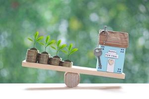 Model house with Trees growing on stack of coins money on wood scale seesaw with natural green background,Business investment and real estate concept photo