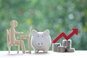 investment and business concept,Man using laptop computer and piggy banks with stack of coin money on natural green background,Investors strategy photo