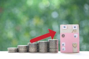 Mortgage,Red arrow graph on stack of coins money and model house on natural green background,Business investment and real estate concept photo