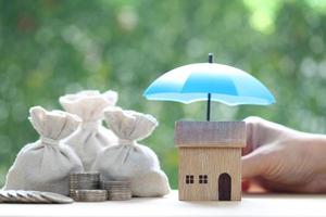 Protection, Model house under the umbrella and coins money in the bag on natural green background, Finance insurance and Safe investment concept photo