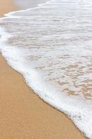 White bubbles of sea waves on sandy beach photo