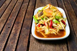 Spicy papaya salad with salted crab and fermented fish on the wooden background. photo