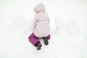 Child plays in snow. Girl in winter. Warm clothes on child. photo