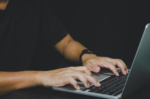 persona que usa la computadora portátil con teclado en la mano sobre fondo negro. foto