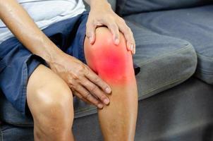 Injury or knee pain of an elderly man on the sofa. photo