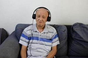 anciano escuchando música con auriculares en el sofá. foto