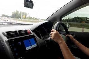 Hand of driving use car steering wheel inside the car. Third person view. Environment of asphalt on rainy time. With blurred of other cars on the road. photo