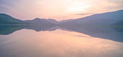 panorama escénico del lago de montaña con reflejo perfecto al amanecer. hermoso paisaje montañoso con cielo rosa pastel con colinas en el fondo y reflejado en el agua. naturaleza lago paisaje foto