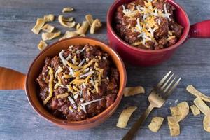 homemade chili in bowls with cheddar cheese and corn chips photo
