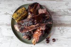 costillas a la barbacoa con mazorcas de maíz en un plato con salsa plana foto