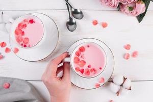 Pink matcha with rose petals on white background. Female hand holds a cup with trending vegan tea. Relaxing drink in the sleepy time. photo