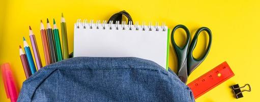 Flat lay student backpack and office supplies on yellow background. Back to school concept. Place for text. photo