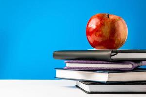 Back to school concept. A stack of books and an apple on blue background. Place for text. photo