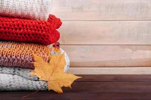 pila de cálidos suéteres de punto. concepto de otoño. puentes de lana y hoja de arce sobre fondo de madera. foto