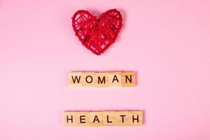 letras de madera y corazón rojo sobre fondo rosa. la salud de la mujer. foto