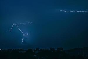 Lightning in sky over city. Bright flashes on dark night. Thunderclouds and electricity discharges in atmosphere. photo