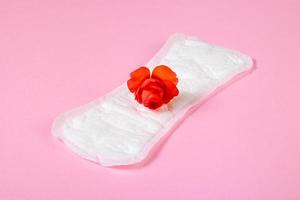 Sanitary pad and red flower on pink background. Menstruation concept. photo