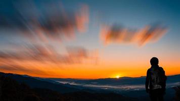 joven fotógrafo hipster sosteniendo la cámara con puesta de sol en el fondo natural de la montaña. foto