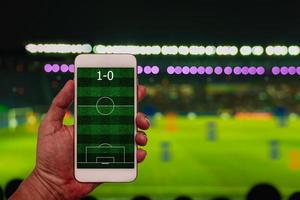 Hand holding smartphone with football field on blur soccer stadium background. photo
