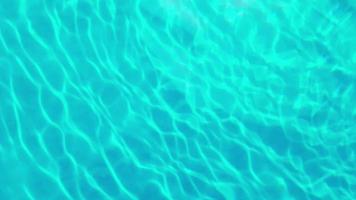 defocus wazig transparant blauw gekleurd helder kalm water oppervlaktetextuur met spatten en bubbels. trendy abstracte natuur achtergrond. watergolven in zonlicht. close-up blauwe water achtergrond. video