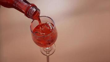 Closeup pouring red sweet water into glass with ice water on orange background. video