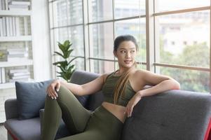 fit beautiful asain woman in sportswear sitting and relaxing on sofa after workout, health and exercise concept photo