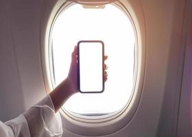 Close up woman hand holding smartphone over window aircraft background , transportation technology concept photo