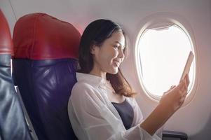 joven hermosa mujer está usando un teléfono inteligente en el concepto de avión, viajes y vacaciones foto