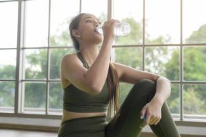 mujer joven fitness en ropa deportiva bebiendo agua después de hacer ejercicio en casa, saludable y estilos de vida. foto