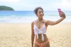 joven mujer hermosa en bikini escuchando música y usando un smartphone en la playa, verano, vacaciones, vacaciones, concepto de estilo de vida.
