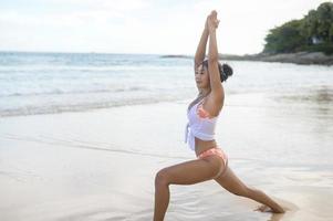 Young asian woman in bikini doing yoga on the beach, health and meditation concept photo