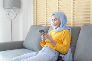 Young happy muslim woman relaxing and using smartphone in living room. photo