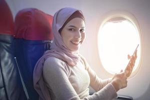 Young muslim woman wearing hijab using smartphone onboard, travel and holidays concept photo