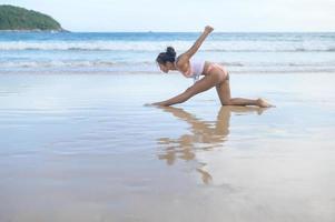 Young asian woman in bikini doing yoga on the beach, health and meditation concept photo