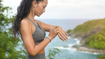 Beautiful fit woman in sportswear using smartwatch and exercising on seaside mountain peak, Health and Travel concept. photo