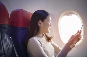 joven hermosa mujer está usando un teléfono inteligente en el concepto de avión, viajes y vacaciones foto