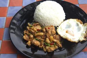 Basil, chicken, fried egg, Thai food The house style is not upscale in a black ceramic plate placed on a plaid concrete table. Ready to serve and delivery photo