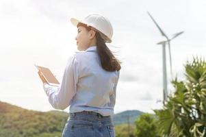 Female engineer working on the seaside wearing a protective helmet over electrical turbines background. photo