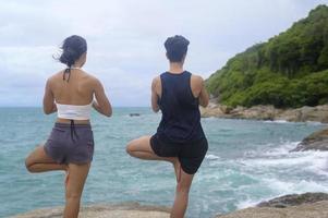 hombre y mujer jóvenes en ropa deportiva haciendo yoga en la roca en el concepto de playa, salud y meditación foto