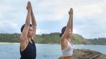 Young man and woman in sportswear doing yoga on the rock at seaside, health and meditation concept photo